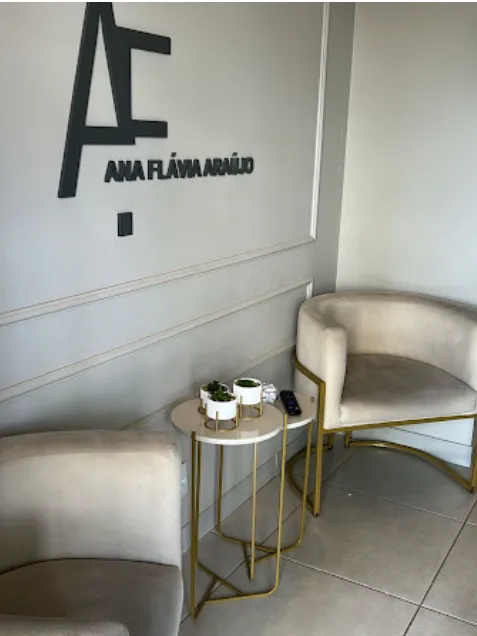 Recepção com o monograma AF na parede, duas poltronas claras de pé dourado e uma mesinha com plantas