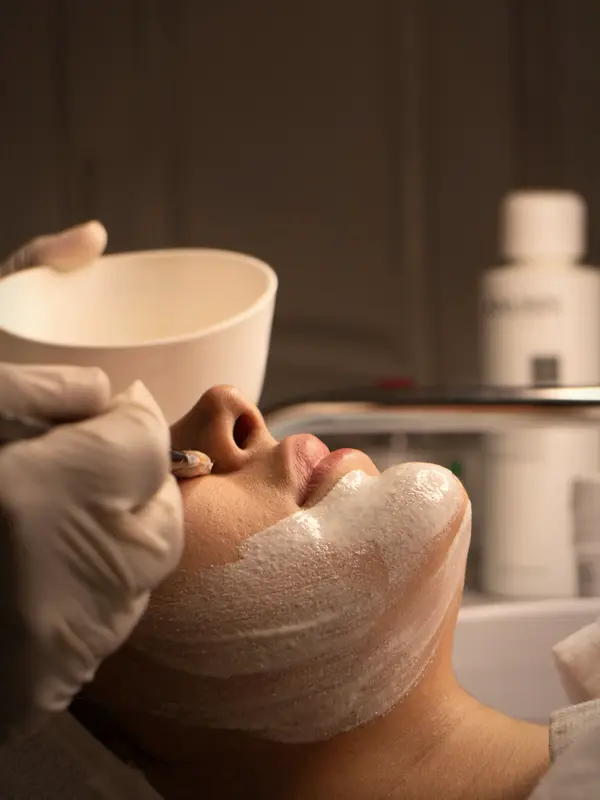 Máscara facial sendo aplicada com pincel no rosto de uma cliente